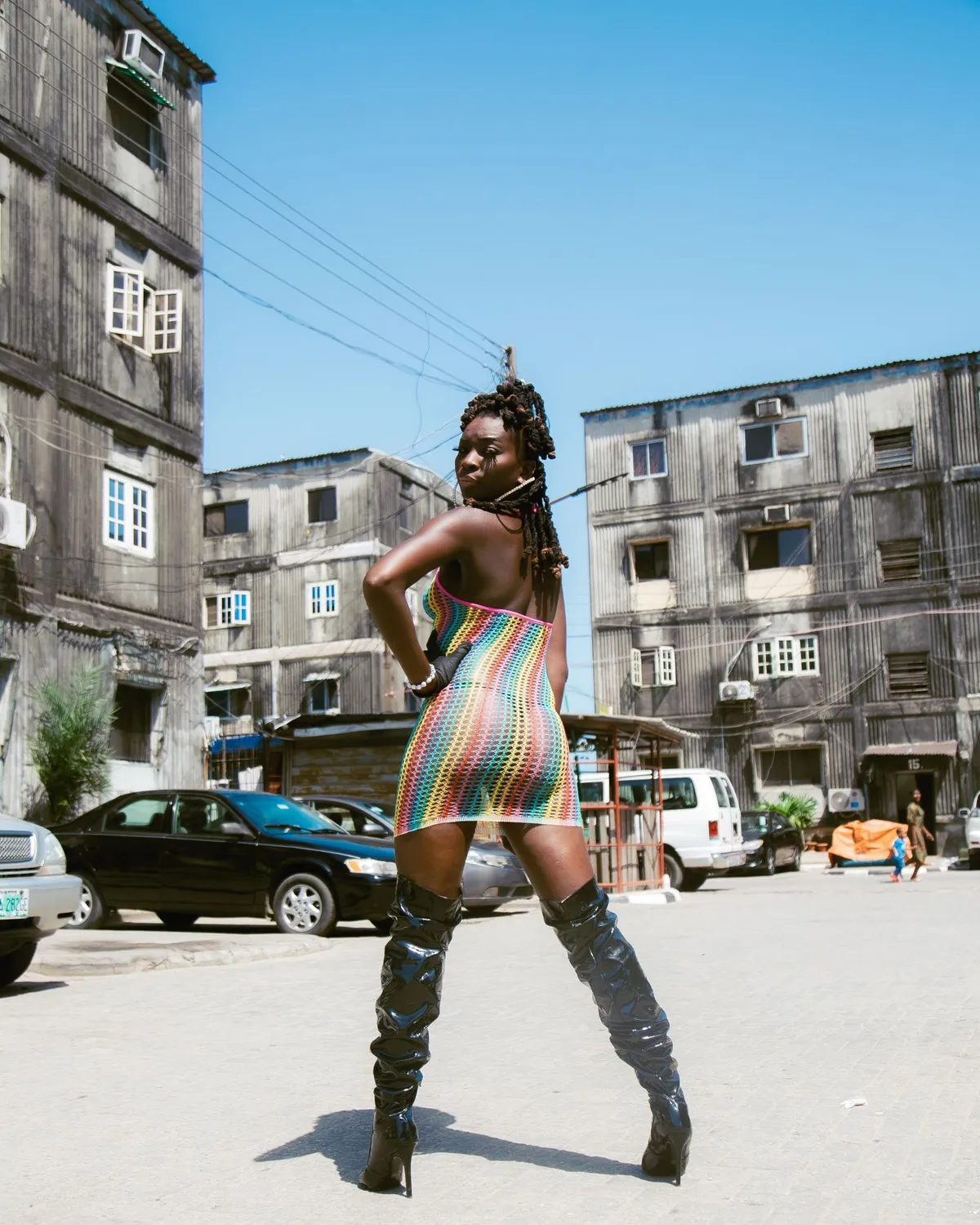 A woman in a colorful dress and boots standing on a city street.