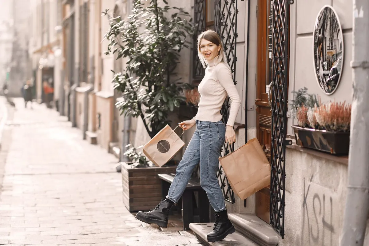 A woman in a cream blouse and jeans carrying shopping bags on a city street.
