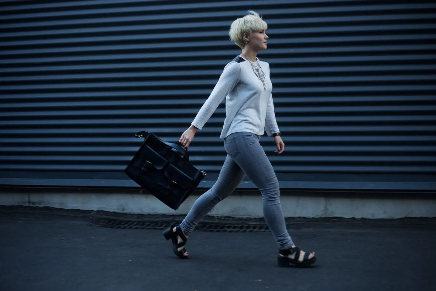 A woman carrying a dark structured bag along a city pavement.
