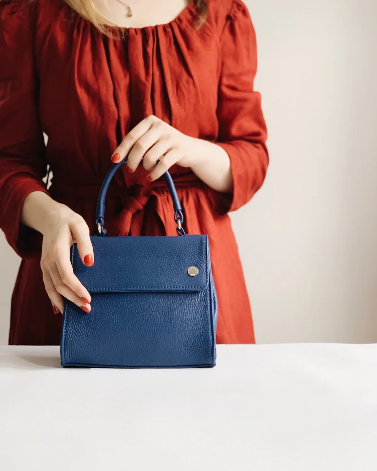 A woman in a rust-colored blouse holding a structured blue bag.