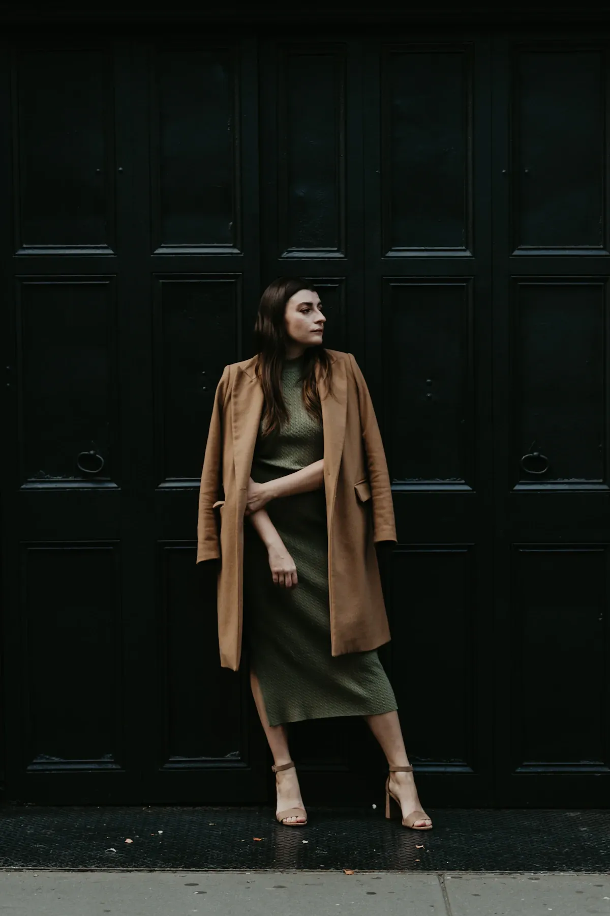 A woman in a brown coat beside a dark wooden doorway.
