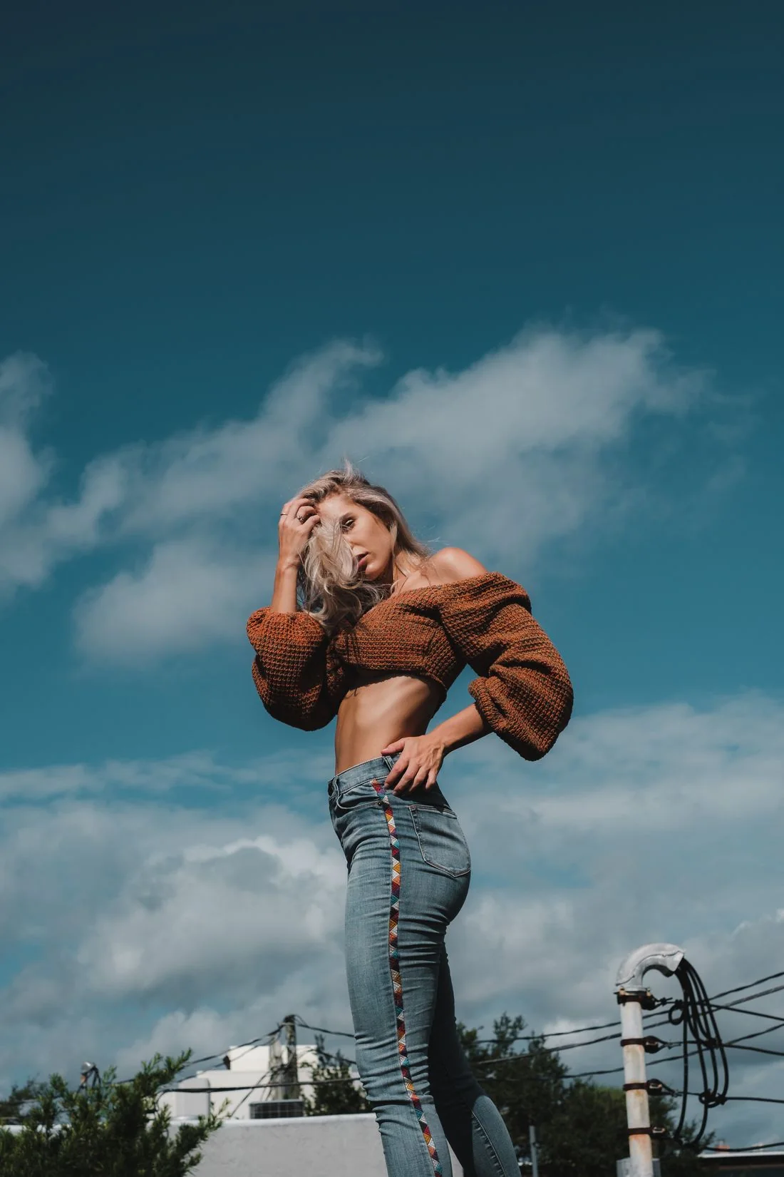 A woman in a brown knit top and jeans beneath a blue sky.