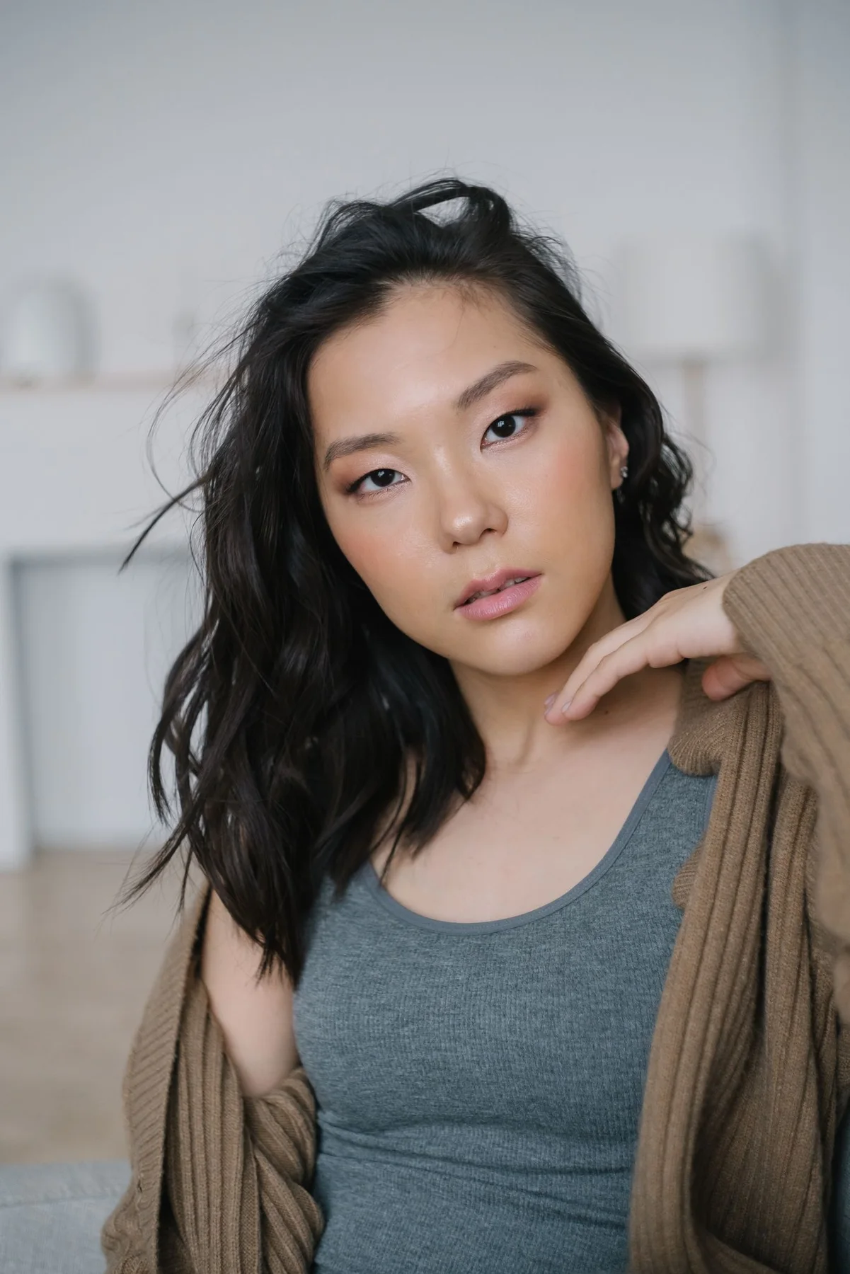 A woman in an open brown cardigan over a grey tank indoors.