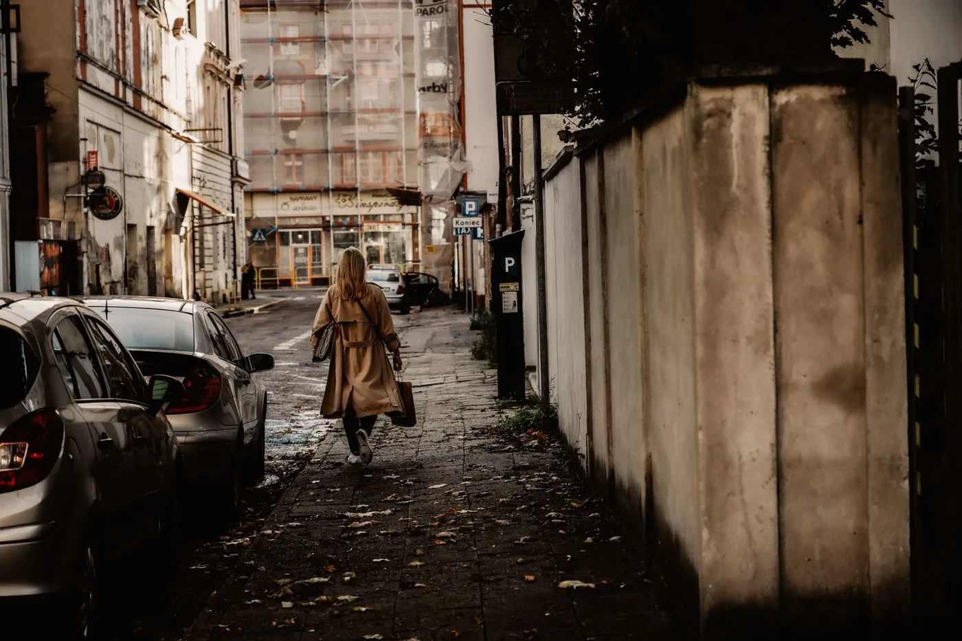 A woman in long outerwear on a narrow city street.