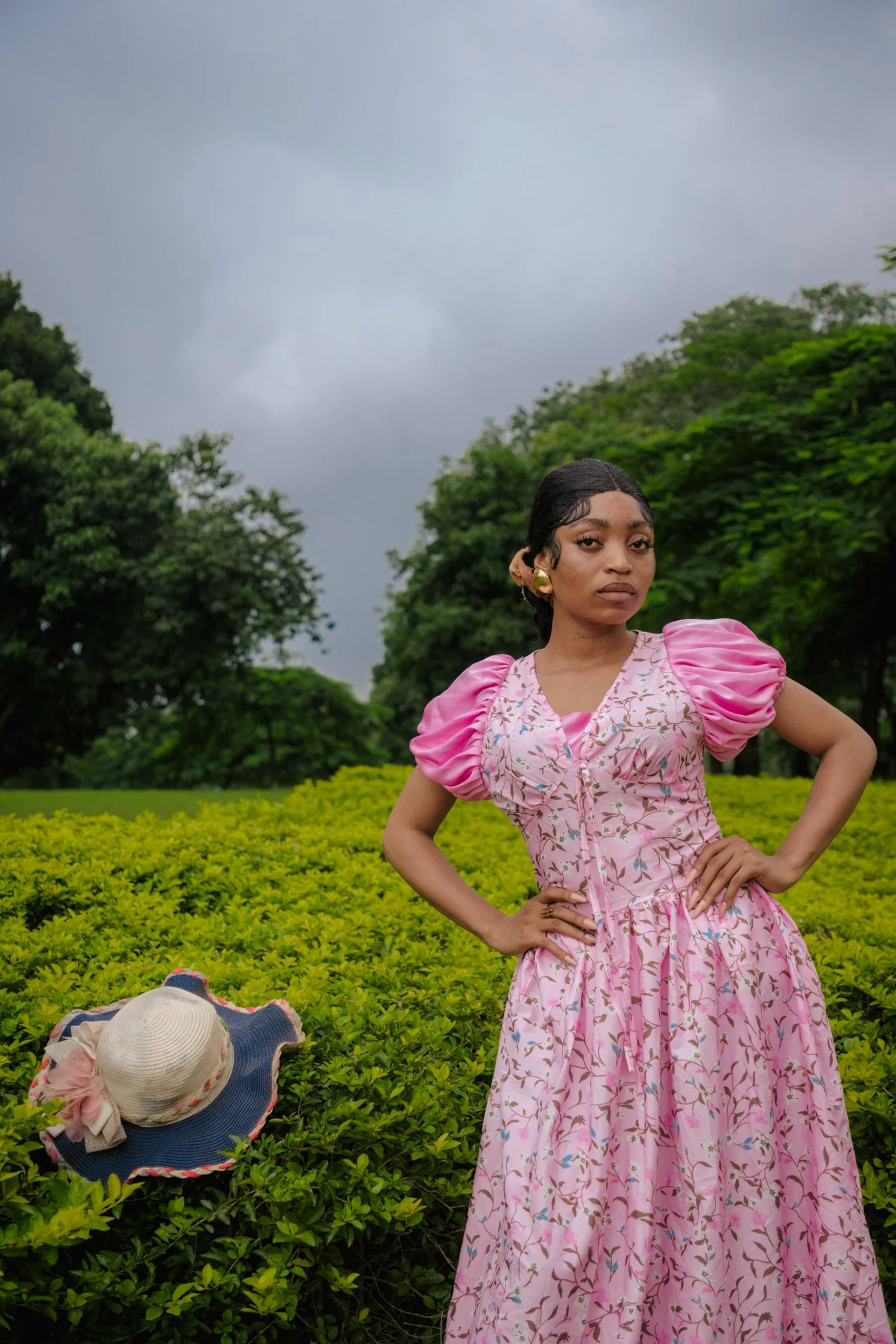 A woman in a pink floral dress in a leafy garden.