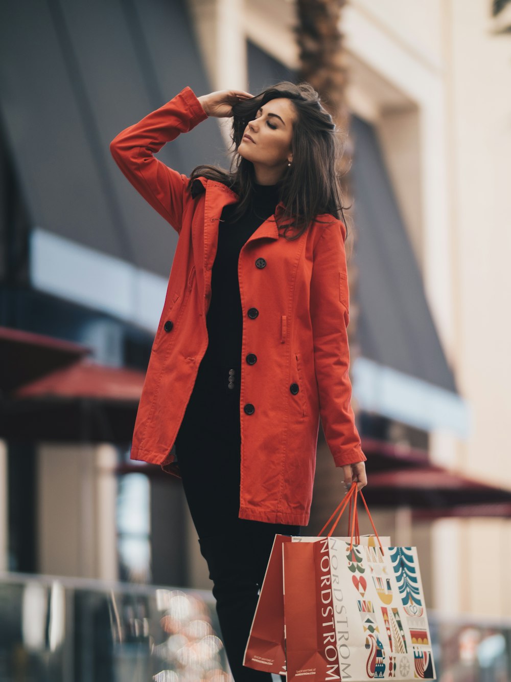A woman in a red coat over dark clothes on a city street.