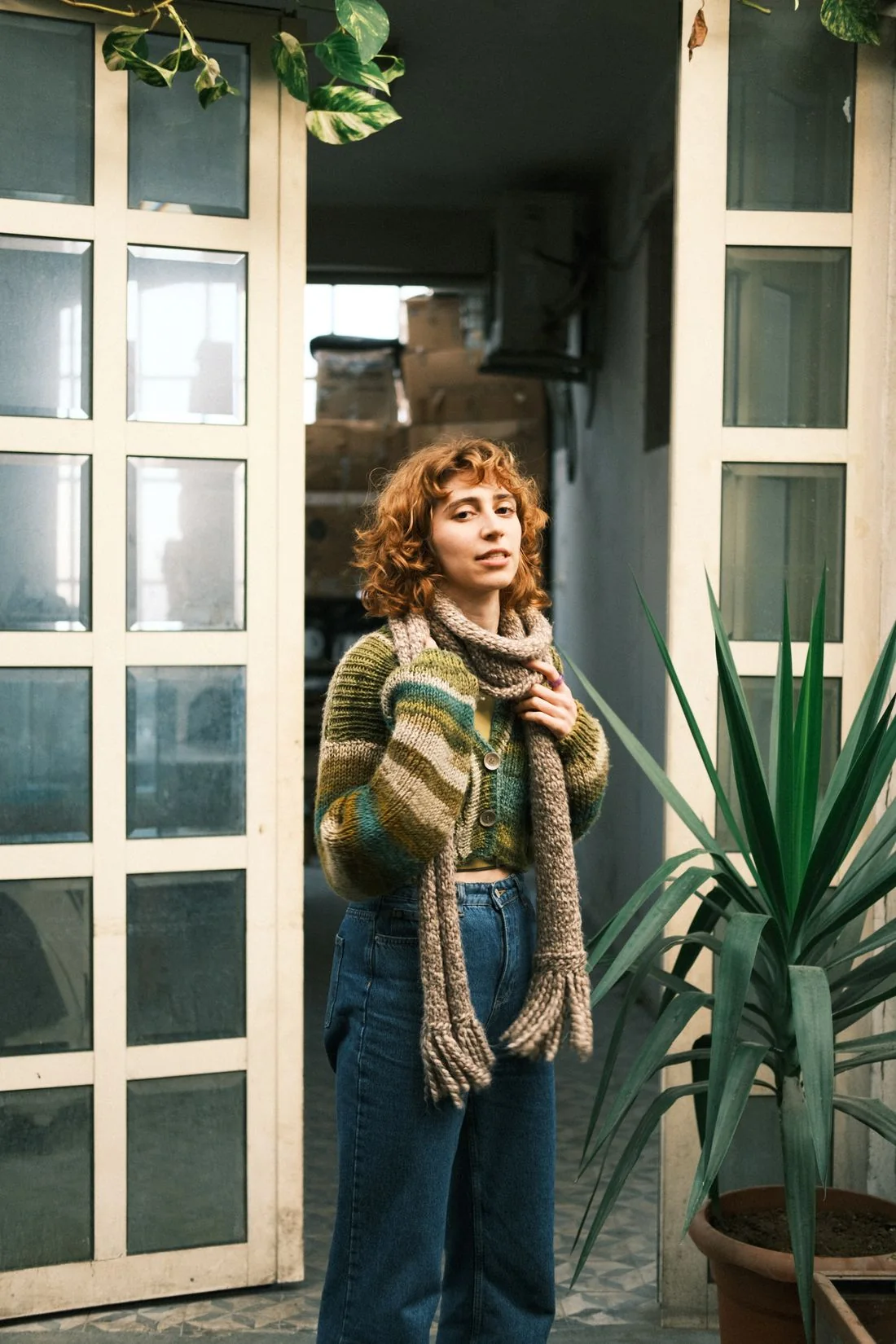 A woman wearing a knit top and scarf beside a glazed doorway.
