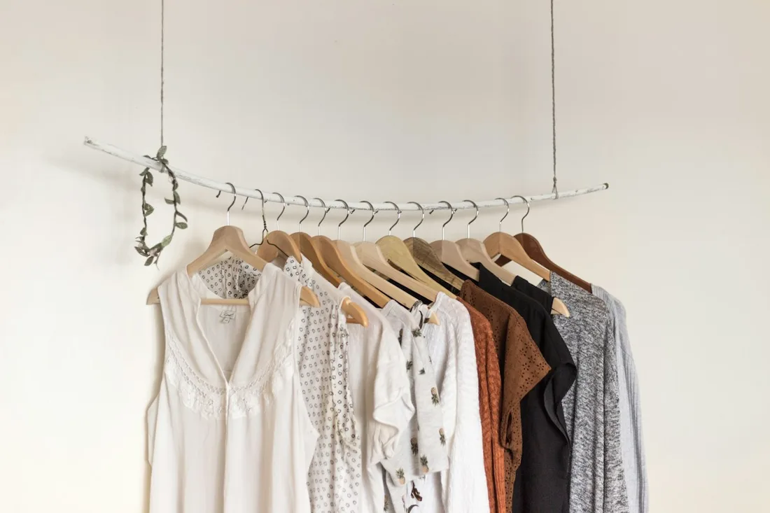 Pale and dark garments arranged on wooden hangers on a rail.