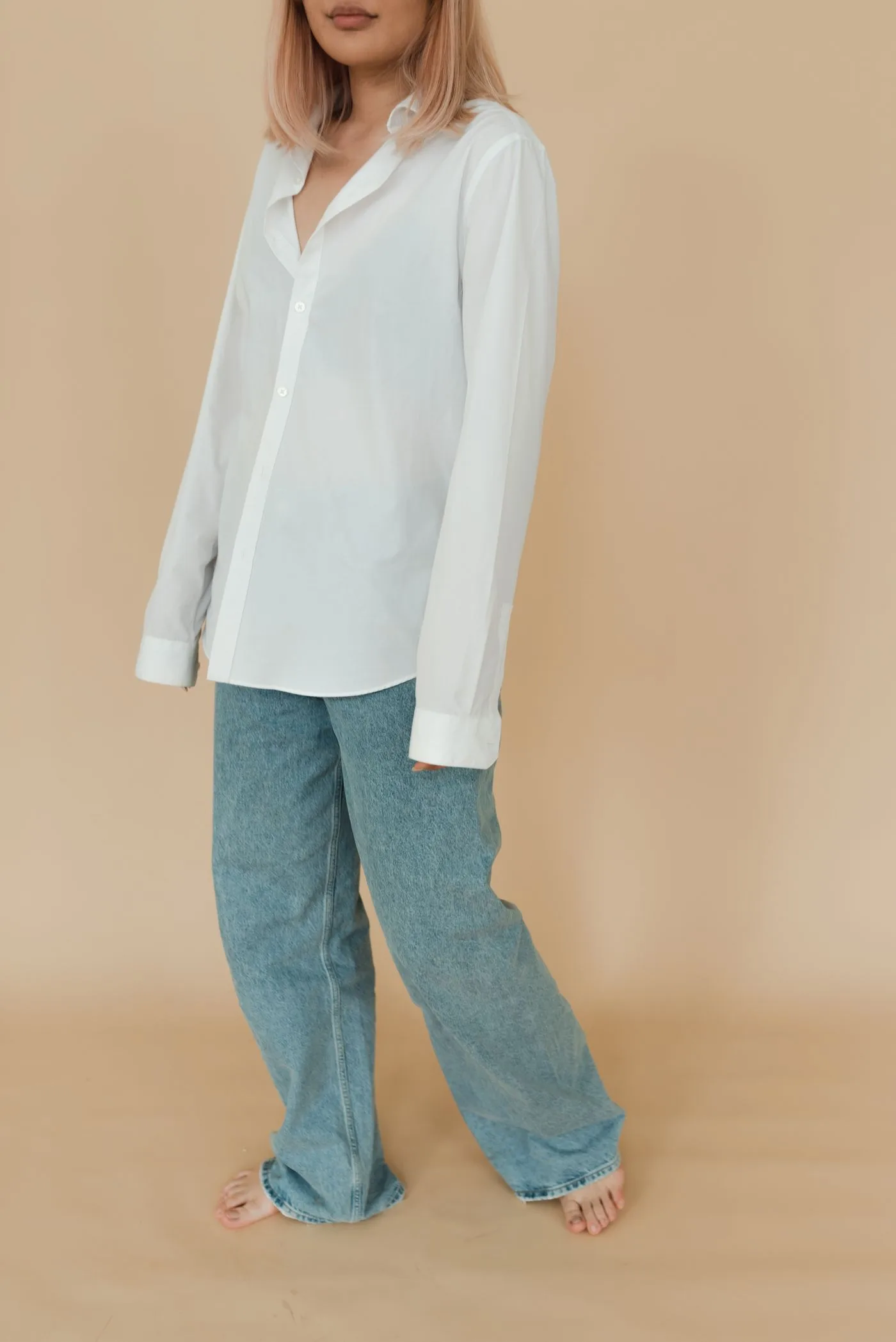 A woman in a loose pale shirt and jeans against a plain warm background.