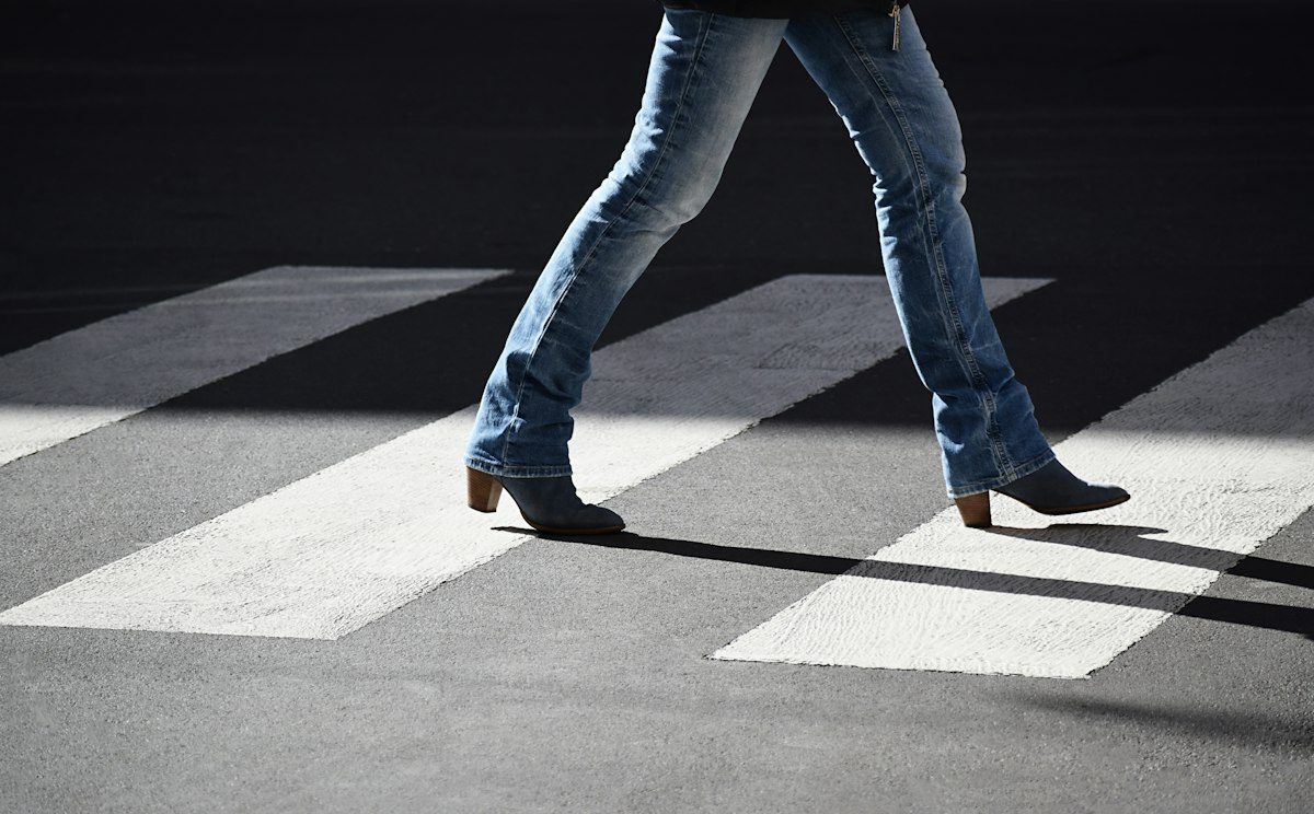 Blue jeans and dark footwear crossing a marked city pavement.