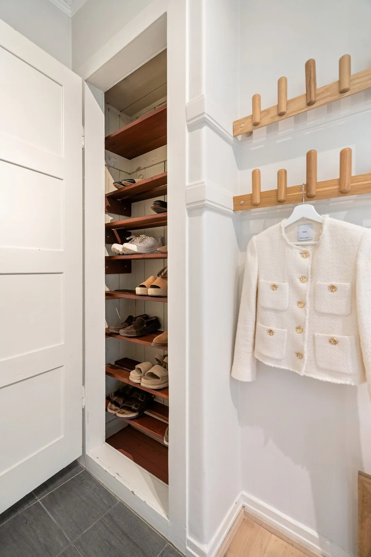 A pale jacket on wall hooks beside an open clothing cupboard.