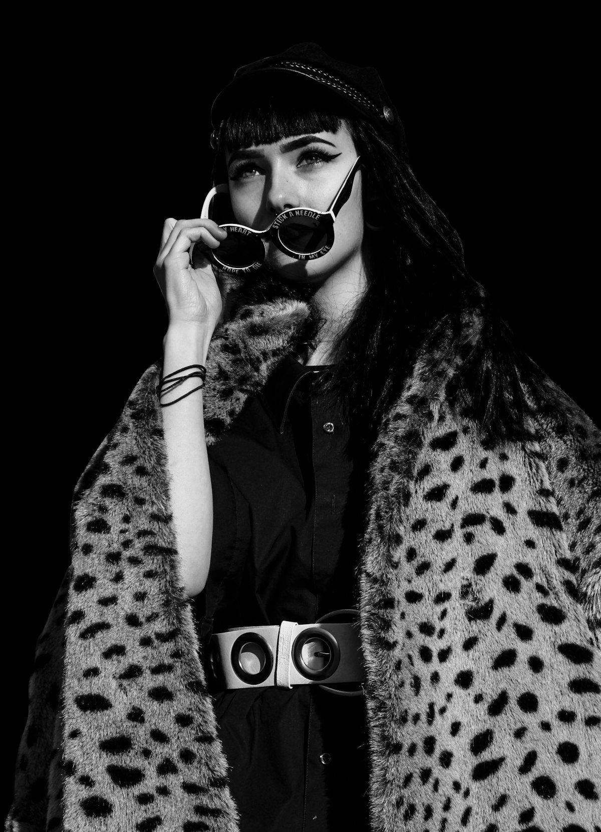 A monochrome portrait of a woman wearing animal-print outerwear with a dark hat and sunglasses.