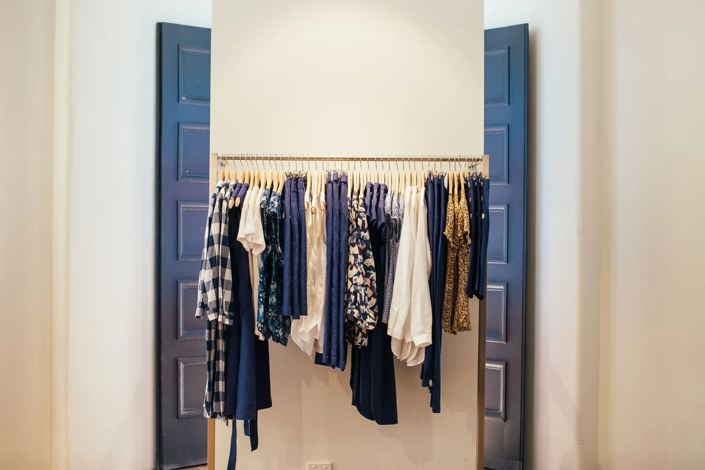 Pale and dark clothes hanging on a rail between tall doors.