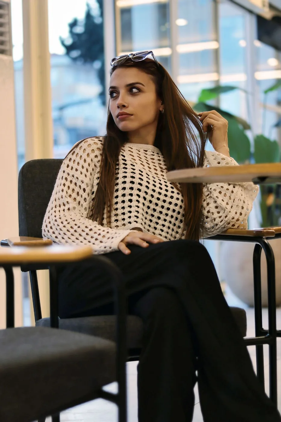 A woman wearing a pale open-textured knit over a dark layer with black trousers at a cafe table.