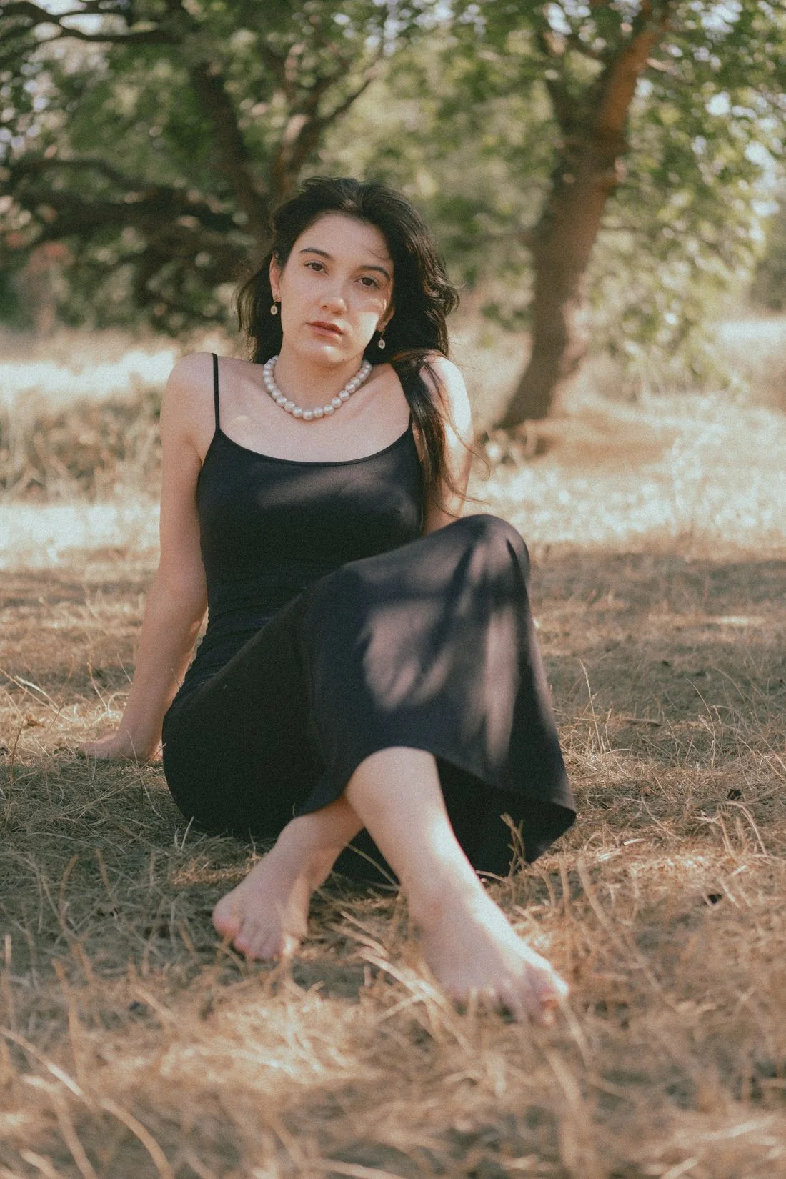 A woman wearing a black slip dress while seated on grass.