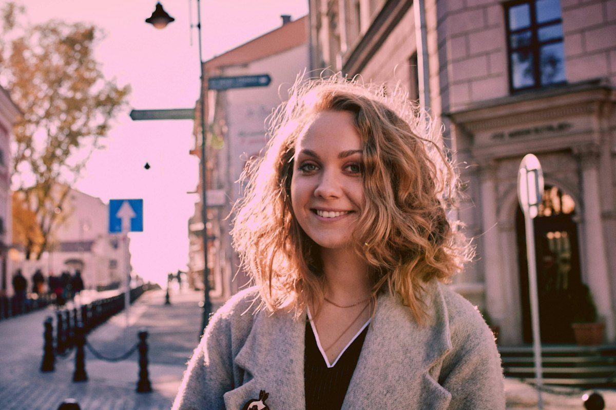 A woman wearing a pale outer layer over a dark top on a city street.