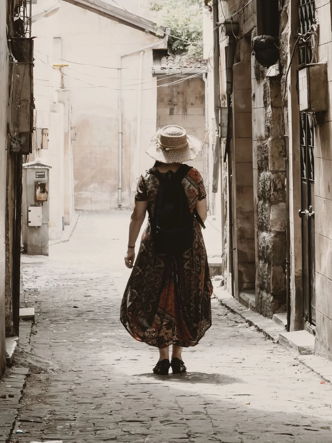 A woman wearing a floral maxi dress on a cobblestone street.