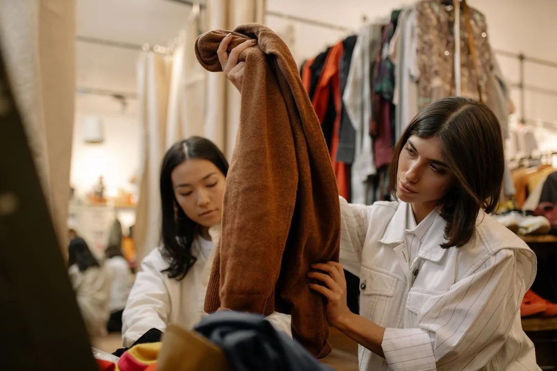 Two women examining garments in a secondhand clothing shop.