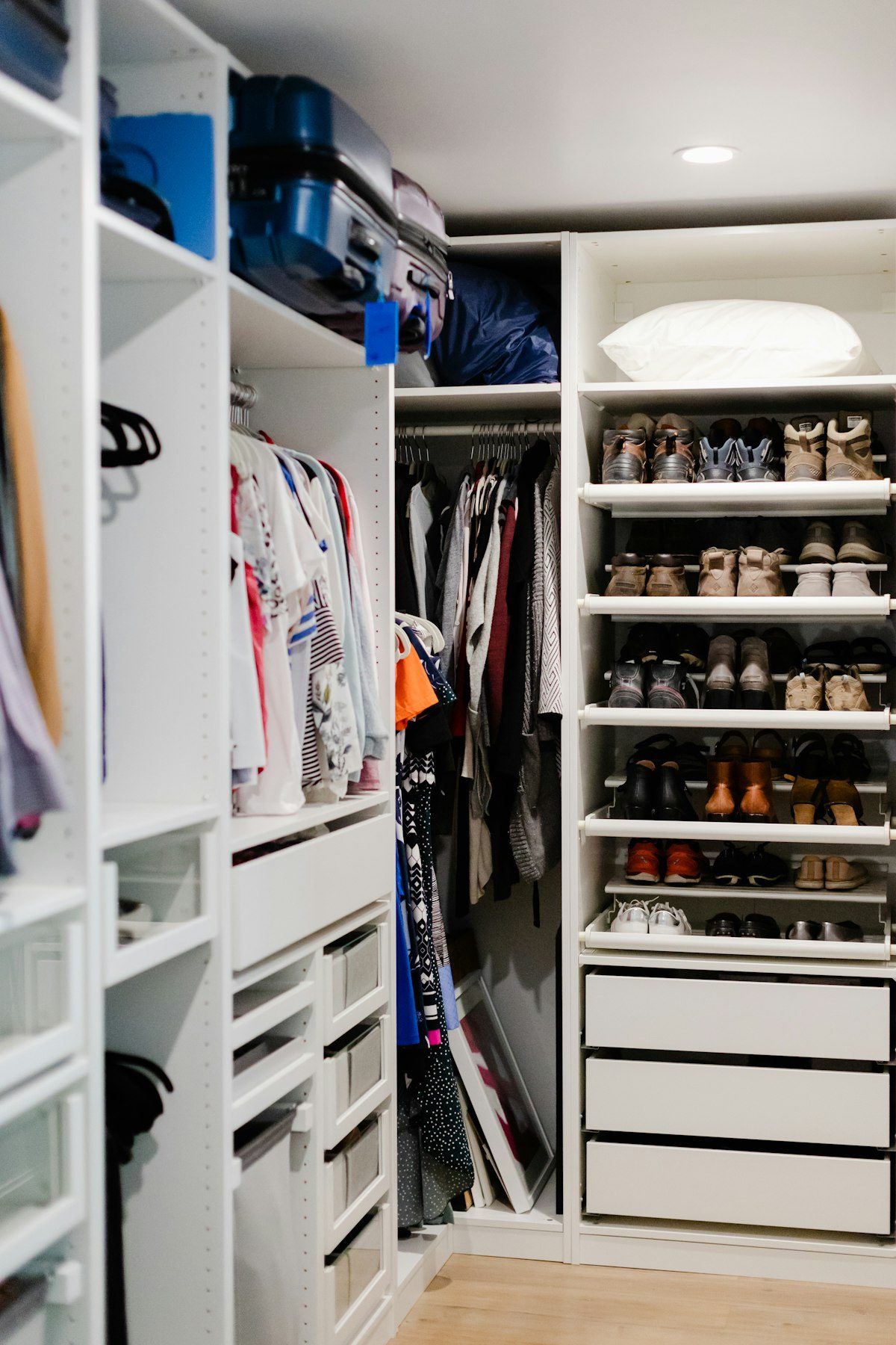 A white walk-in wardrobe with shelves, hanging clothes and shoes.