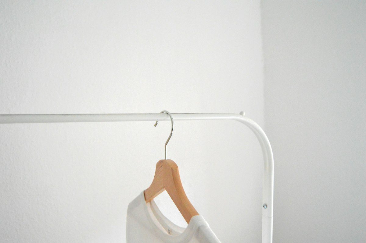 A pale garment on a wooden hanger against a light wall.