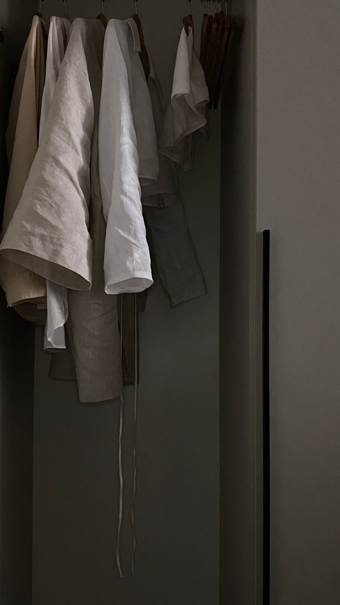 Pale shirts hanging on wooden hangers in a wardrobe.
