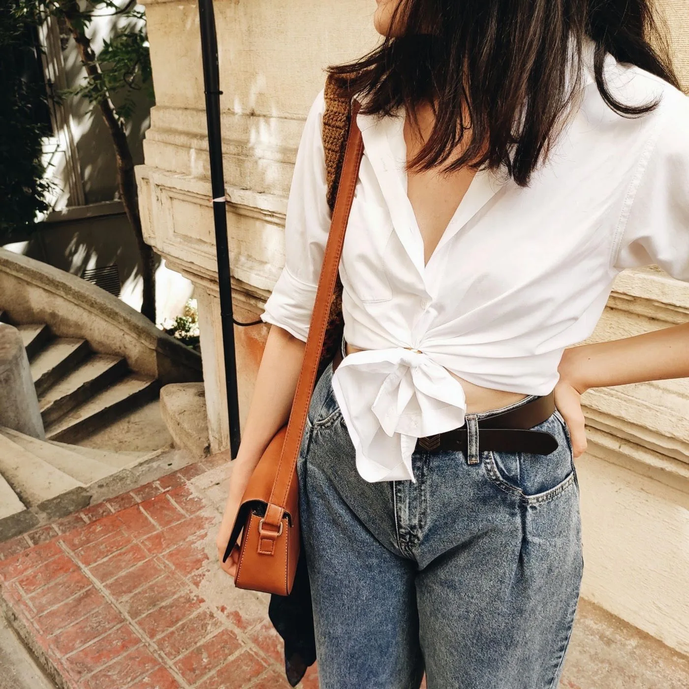 A woman wearing a white shirt tied at the front with blue jeans.
