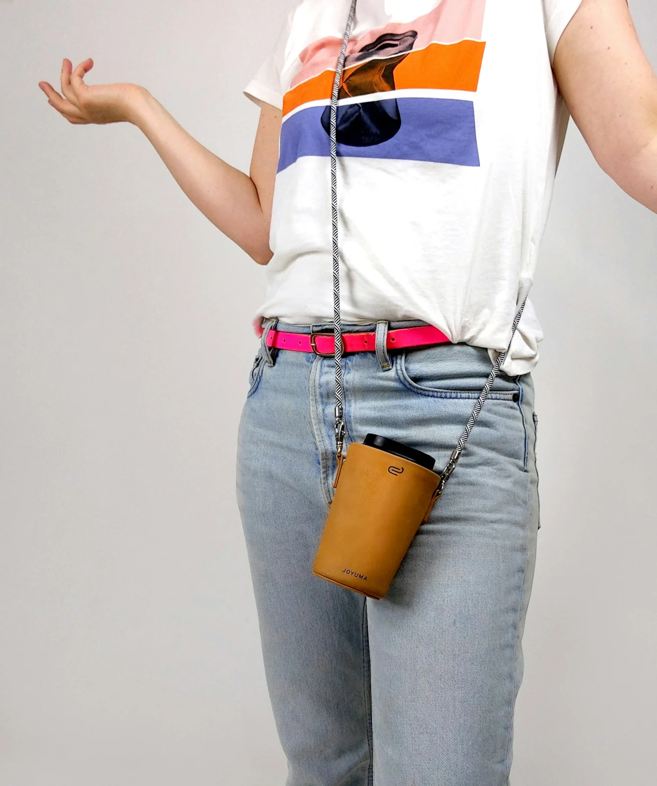 A mustard-colored cup carrier on a crossbody cord over a printed T-shirt and jeans.