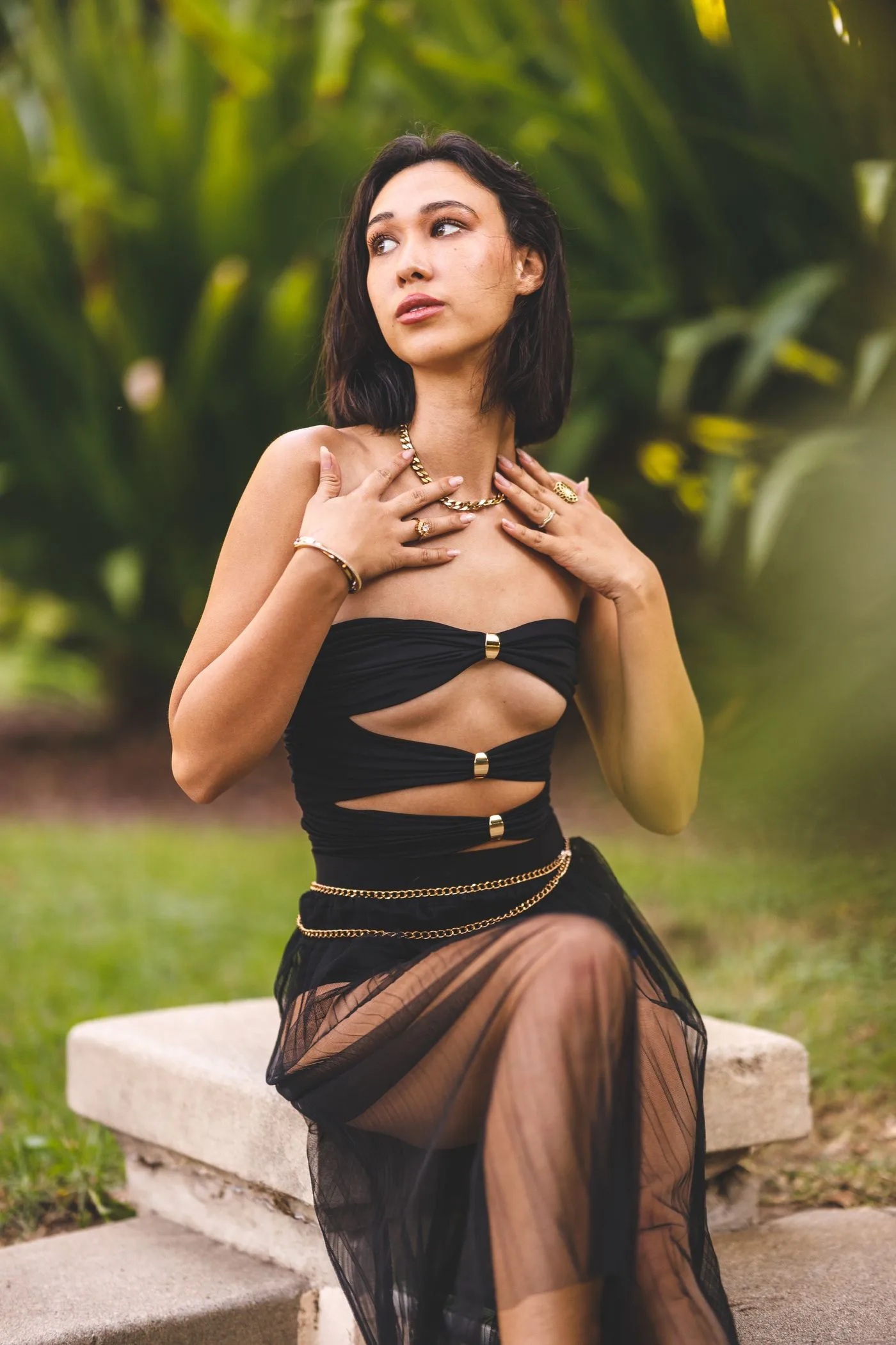 A woman in a dark cutout dress seated outdoors.