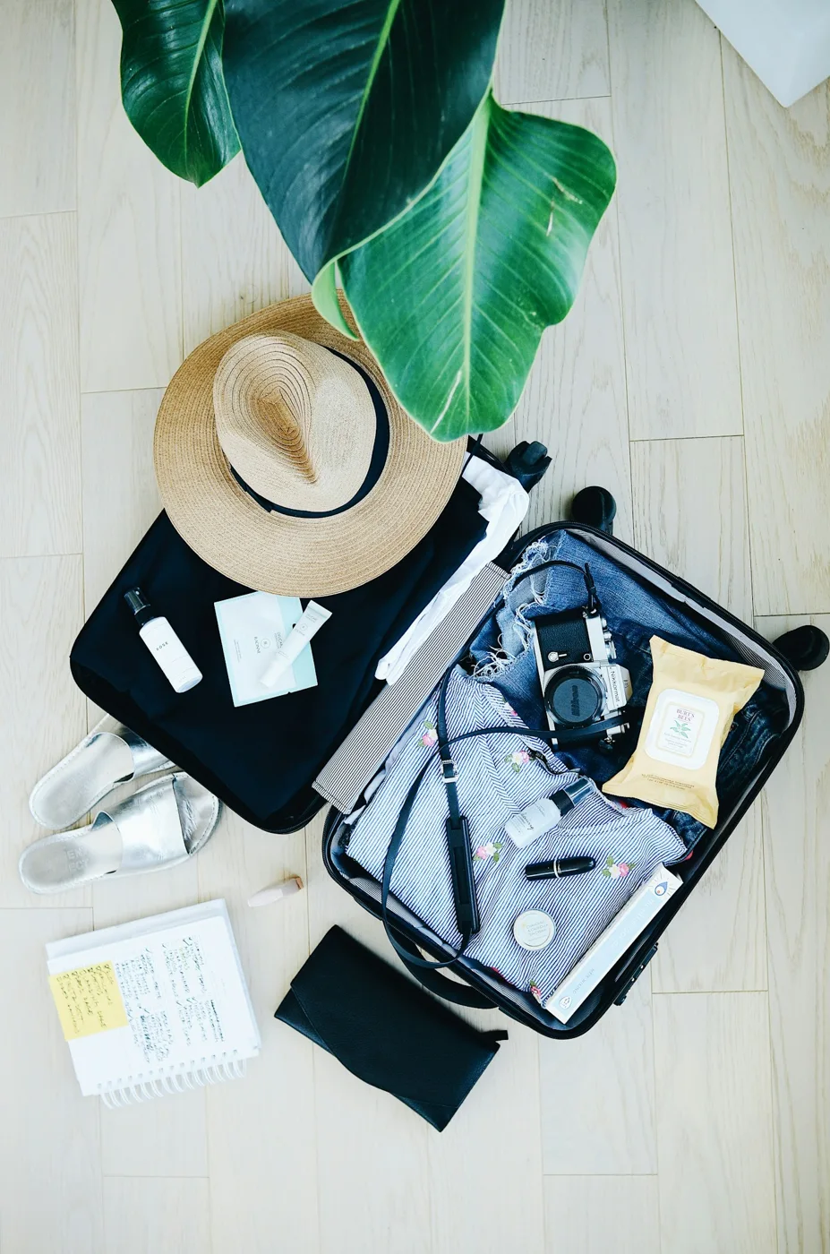 An open suitcase with clothing and a hat nearby.
