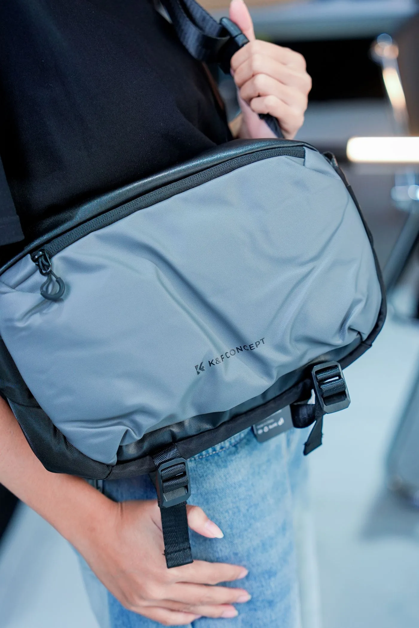 A light-colored messenger bag with dark trim worn over a dark top.