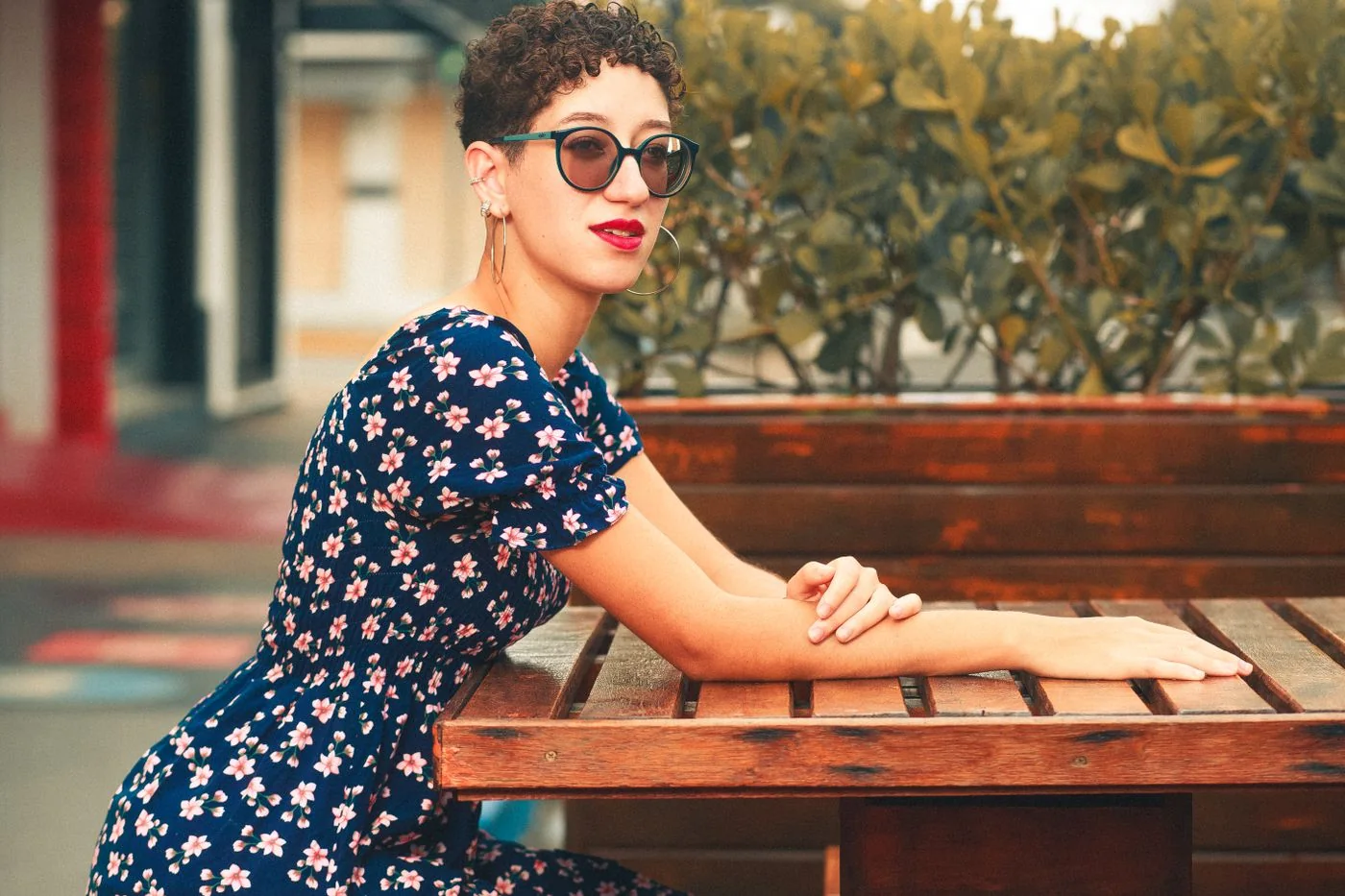 A woman in a floral dress and sunglasses seated at an outdoor table.