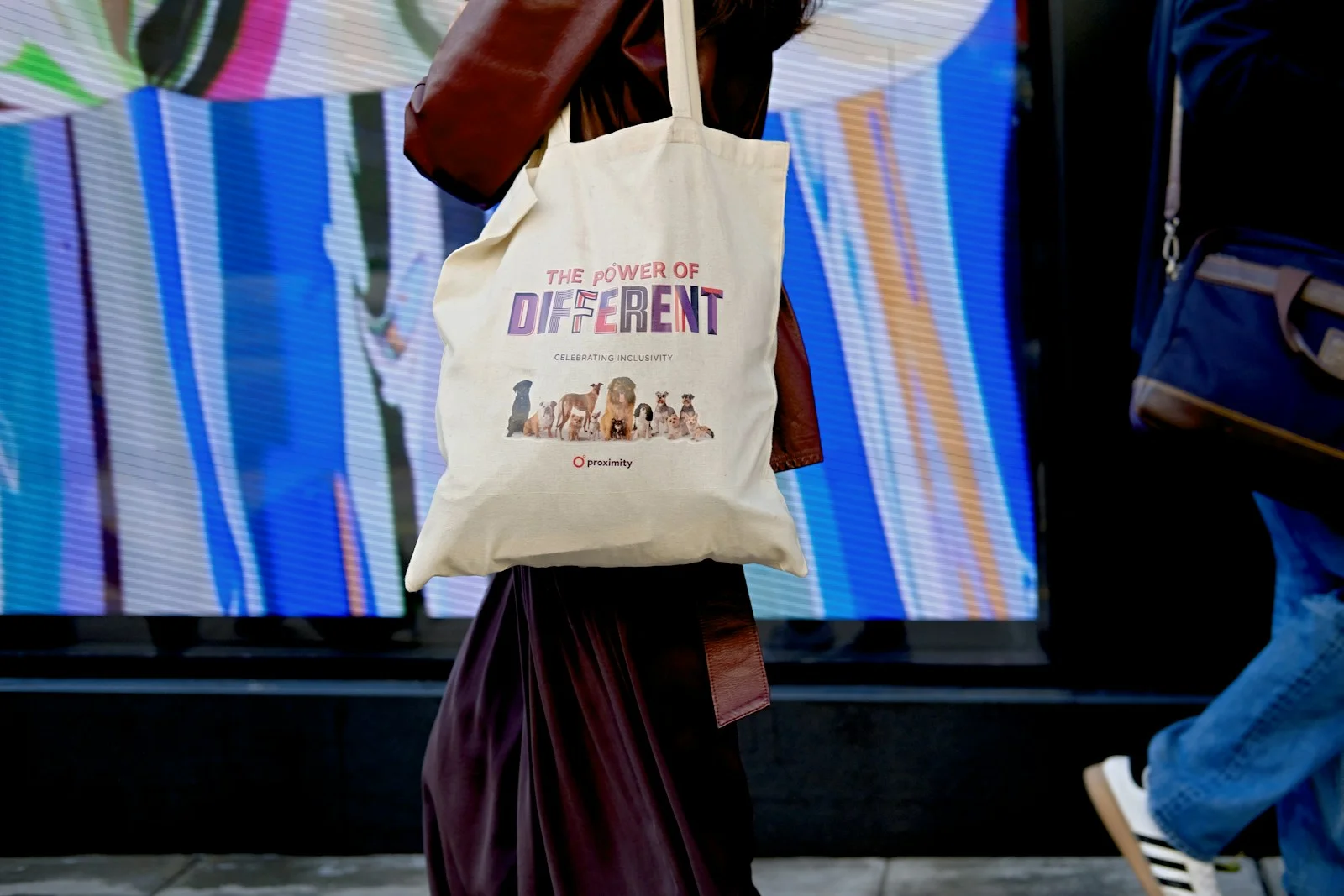 A pale printed tote carried beside a colorful wall.