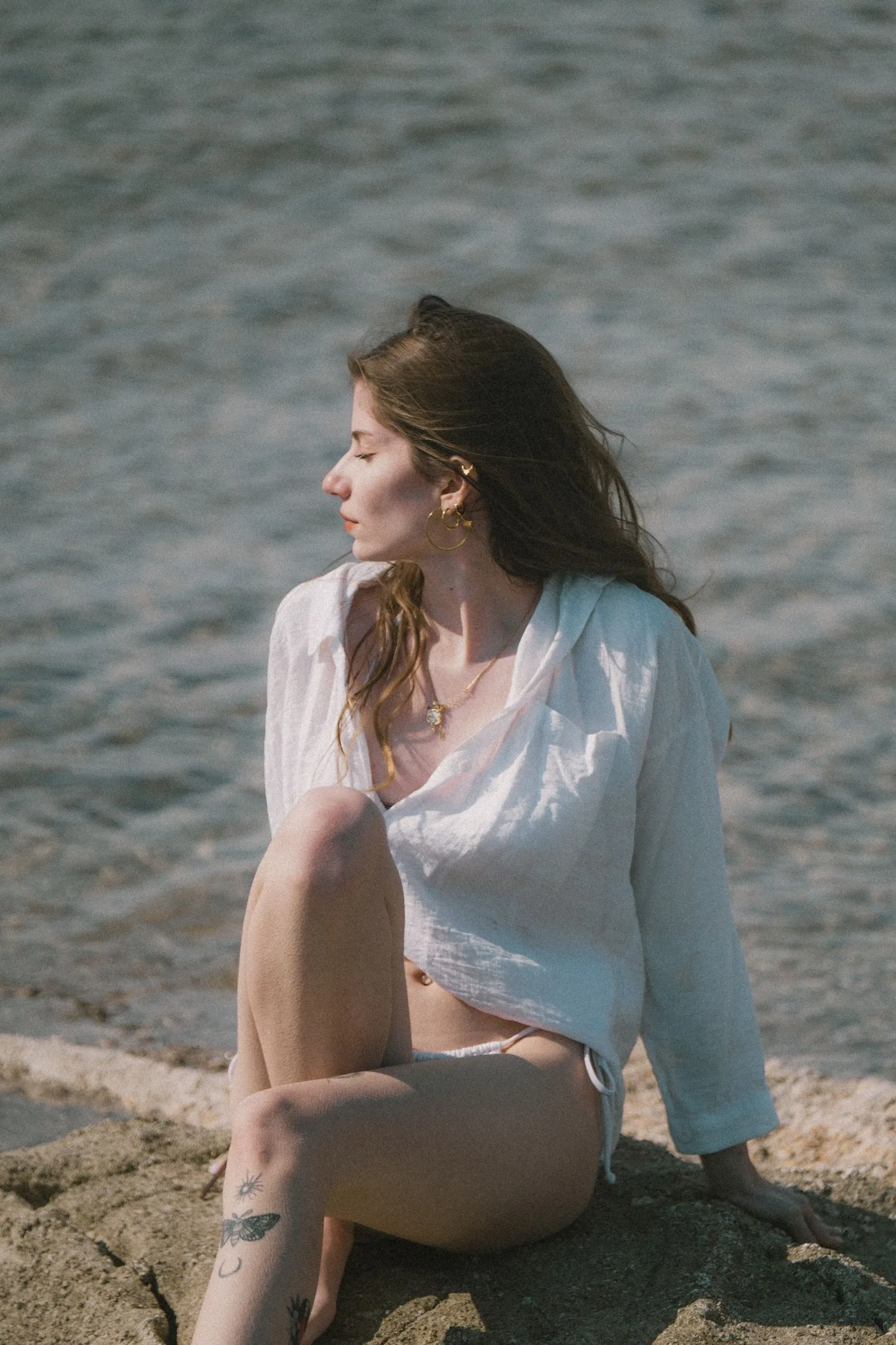 A woman in a pale collared shirt seated beside water.