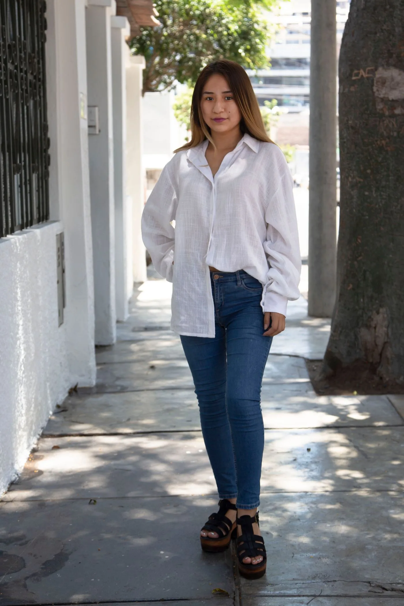 A woman wearing a pale shirt and blue jeans on a city pavement.