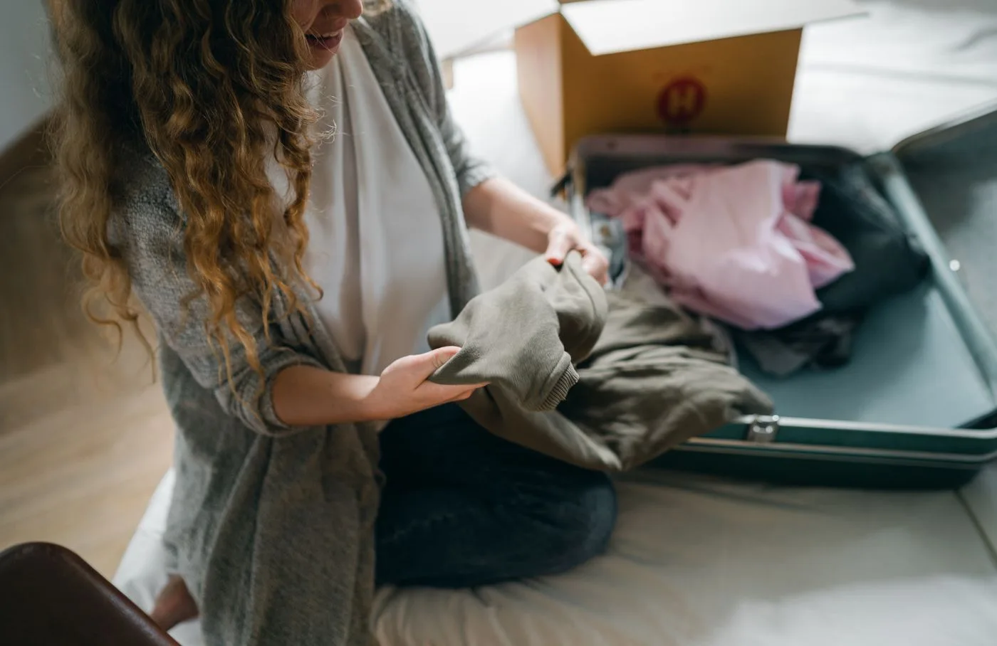 A woman handling clothing beside an open suitcase on a bed.